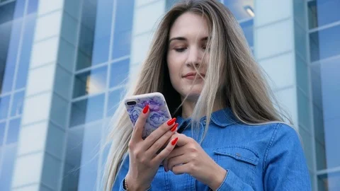 Beautiful lady using her mobile phone, smarthone, texting in front of a modern 動画素材 101233794