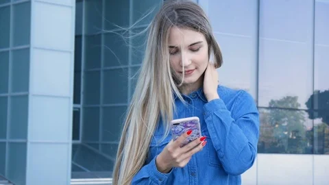 Beautiful lady using her mobile phone, smarthone, texting in front of a modern 스톡 동영상 101234148