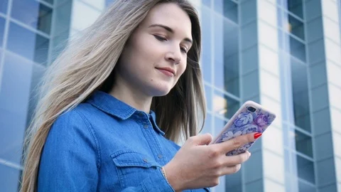 Beautiful lady using her mobile phone, smarthone, texting in front of a modern 스톡 동영상 101237204