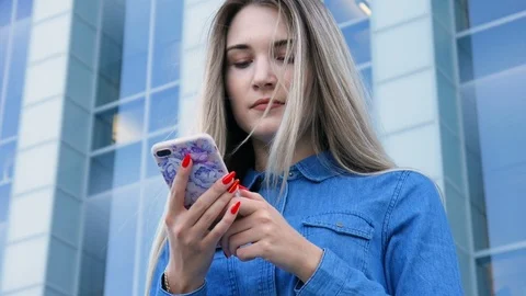 Beautiful lady using her mobile phone, smarthone, texting in front of a modern 스톡 동영상 101237474