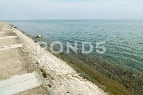 Beautiful lake shore nature view with concrete embankment and wall leading i Stock Photos