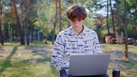 In a beautiful large park student guy using a laptop to studying at fresh air he Stock Footage 133637607