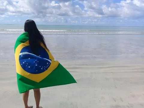 A beautiful latin woman with bikini holding a brazilian flag at the beach Stock Photos