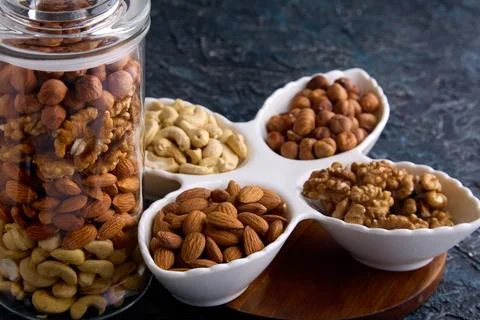 Beautiful layout of nuts on a gray background in white dishes and a glass jar Stock Photos