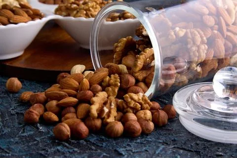 Beautiful layout of nuts on a gray background in white dishes and a glass jar Stock Photos