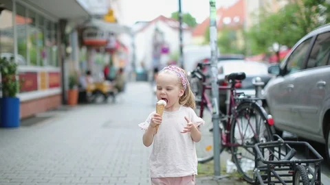 Beautiful little blonde eats ice cream on the street of the city in summer Stock Footage 130171649