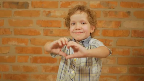 A beautiful little boy makes a heart shape with his hands holding up a love Stock Footage 123734009