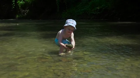 Beautiful Little Boy Throws Pebbles in a Mountain River Stock Footage 65175268