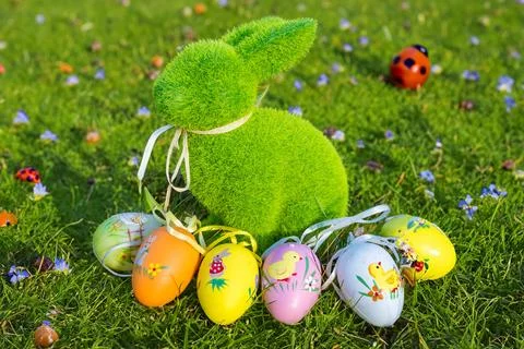 Beautiful little Easter bunny with egg, sitting on green grass with flowers Stock Photos