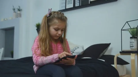 Beautiful little girl playing on a tablet computer sitting on the bed at home Stock Footage