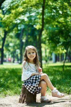 Beautiful little girl sitting in the park on a bright sunny summer day. Stock Photos