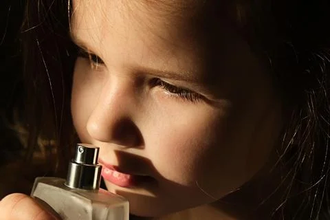 Beautiful little girl sniffs perfume from a bottle, in dark settings Stock Photos