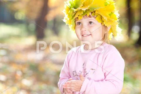 Beautiful little girl in a wreath of maple leaves in autumn forest Stock Photos