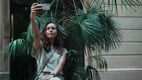 Beautiful long-haired brunette taking selfie while sitting on a street pot with Stock Footage 139351333