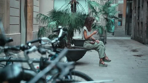 Beautiful long-haired brunette texting message while sitting on a street pot Stock Footage 139442365