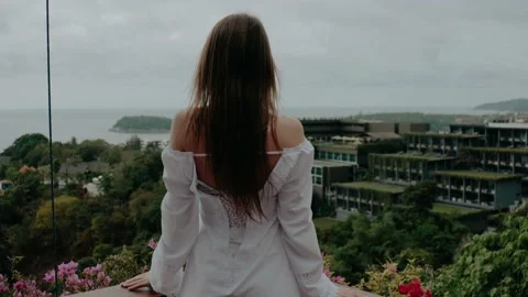 A beautiful long-haired girl in a white dress stands with her back and looks Stock Footage 130282953