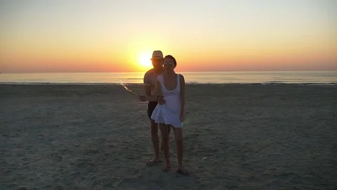 Beautiful lovers dancing on the beach with a firework candle at sunset Stock Footage 71384932