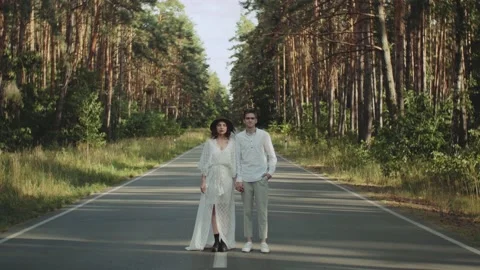 A beautiful loving couple stands in the middle of the road holding hands and Stock Footage