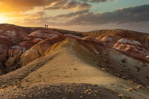 Beautiful low angle shot of two tiny human figures walking towards sunset on  Stock Photos