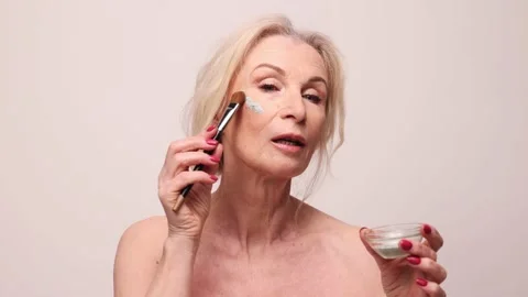 Smoothing out wrinkles.Portrait of an older adult woman with closed eyes  doing a beauty injection. Hands in white gloves hold a syringe.Face lift.  Stock Photo