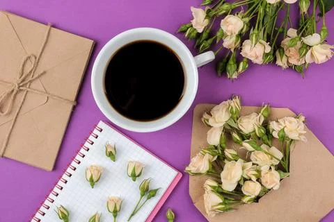 Beautiful mini roses in an envelope with a notepad and a cup of coffee on a b Stock Photos