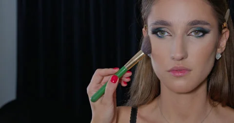 A beautiful model on a dark background is having bright stage makeup applied by Vídeos de archivo 348025413