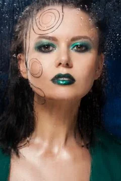 Beautiful model girl stands behind a glass with raindrops. Stock Photos