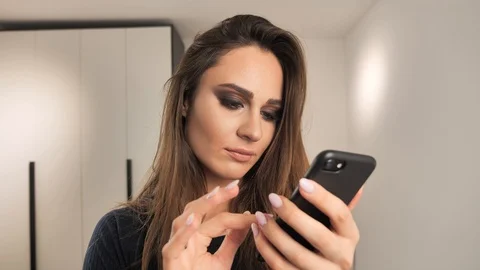 Beautiful model with make-up reading message on smartphone and becoming Stock Footage 120411179
