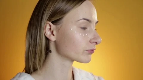 Beautiful model putting face cream on on yellow background Vídeos de archivo 71894624