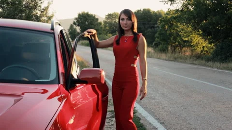 Beautiful model in red jumpsuit posing near the car and smiling Stock-Footage 66816254