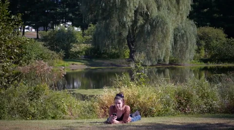 Beautiful model on smartphone lying down in front of lake Stock Footage 40292621