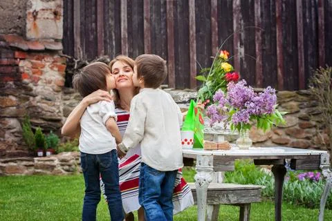 Beautiful mom, having coffee in a backyard, young cute child giving her prese Stock Photos