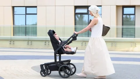 Beautiful mom walking with child in stroller in city. Fashionable family Stock Footage 327783316