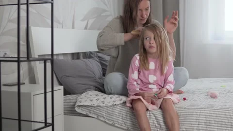 A beautiful mother combs the blonde tangled hair of a little daughter at home Stock Footage 161976795