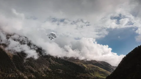 Beautiful movement of clouds over mountain forest slopes and snowy mountain peak Stock Footage 246971615