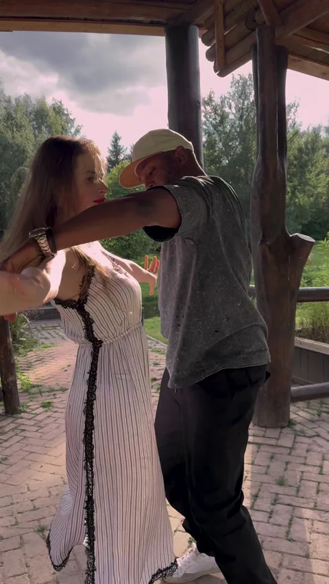 Beautiful multiethnic couple dancing during golden hour in green park. Backlit Stock Footage 329881487