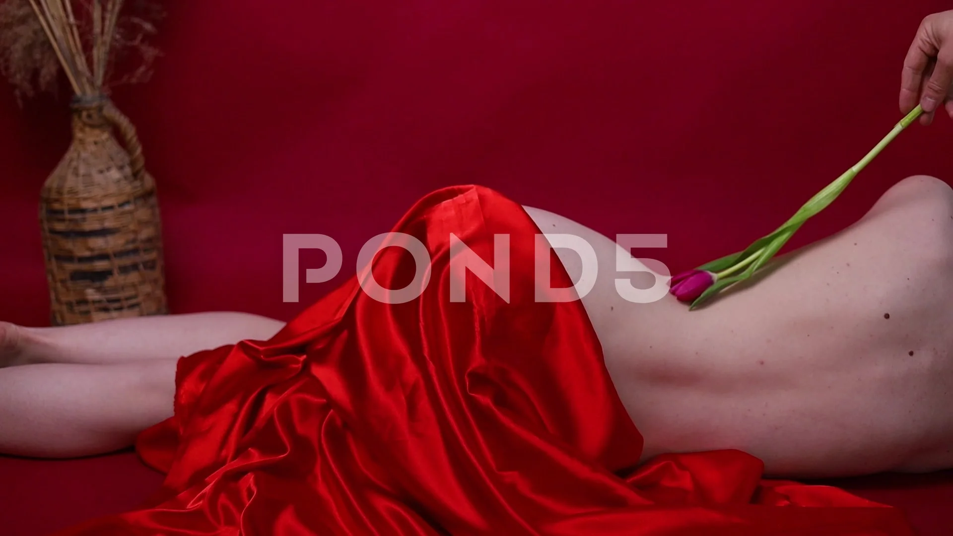 Beautiful naked woman in a red silk cloth posing on red background.