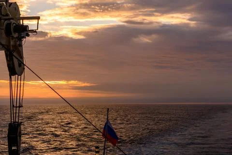 Beautiful ocean sunset under a dramatic sky with a ship and a flag in view Foto stock