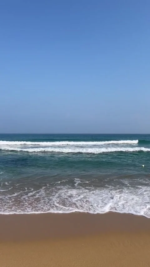 Beautiful ocean waves breaking on sandy beach under clear blue sky vertical view Vidéo 334163373
