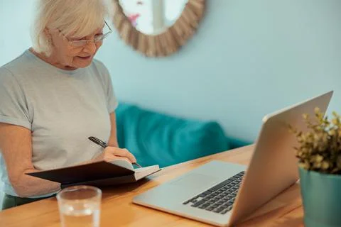 Beautiful older lady taking notes at home Stock Photos