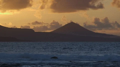 Beautiful orange evening sky with mountain silhouette and ocean in foreground Stock Footage 86464962