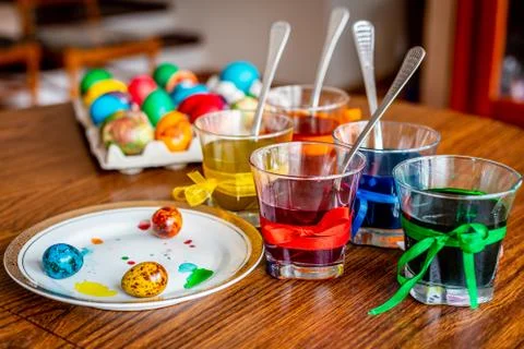 Beautiful painted easter egg, glasses with paints and plate with eggs. Stock Photos