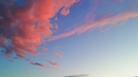 Beautiful pink clouds drift across a clear blue sky during sunset. Stock Footage 339375789
