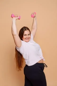 Beautiful plus size model posing with pink dumbbells on beige background Stock Photos