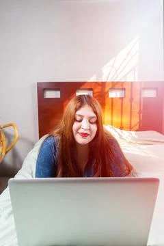 Beautiful plus size model using laptop relaxed lying on her bed Stock Photos