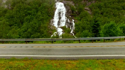A beautiful powerful waterfall flows from a high mountain under the bridge and Stock Footage 152415658