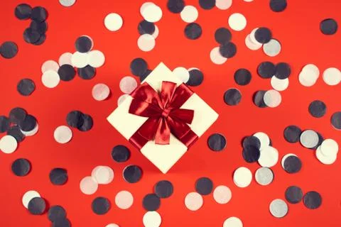 Beautiful present box on red background with confetti. Stock Photos
