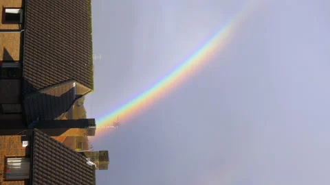 Beautiful rainbow over house rooftops on moody overcast day, vertical footage Stock Footage 147981414