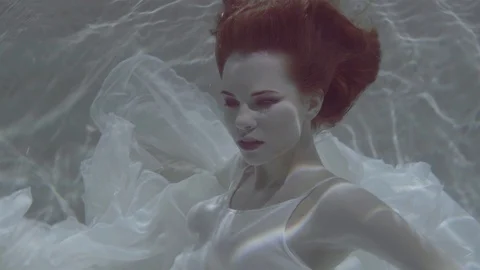 Beautiful Red Haired Woman In A White Dress Swimming Under Water