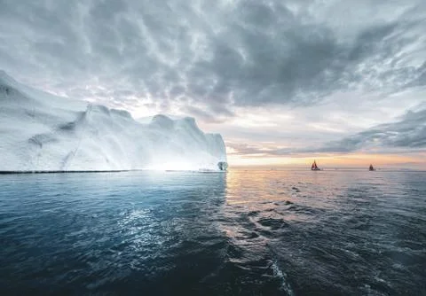 Beautiful red sailboat in the arctic next to a massive iceberg showing the scale Stock Photos